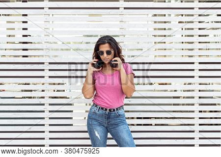 Young Women With Headphones And Sunglasses Stays Near A  Geometric Wall