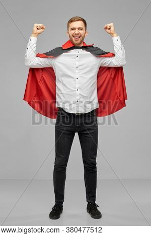 holiday, theme party and gesture concept - happy smiling man in halloween costume of vampire and dracula cape celebrating success over grey background