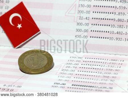 One Turk Lirasi Or Turkish Lira Coin Money On Reverse And Mini Turkey Flag On The Book Bank. Concept