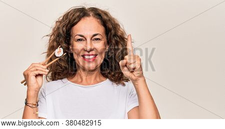 Middle age beautiful  woman eating sushi using wooden chopsticks over white background smiling with an idea or question pointing finger with happy face, number one
