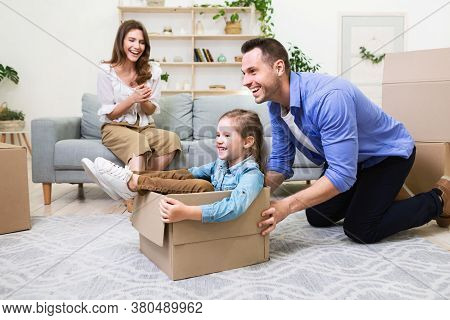 Family Relocation Concept. Dad Riding Little Daughter In Moving Box Having Fun In New Home. Selectiv