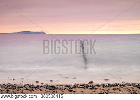 Sunset Over Smooth Water With A View Over Breakwater And Cloudy Skies. Long Shutter Time Photography