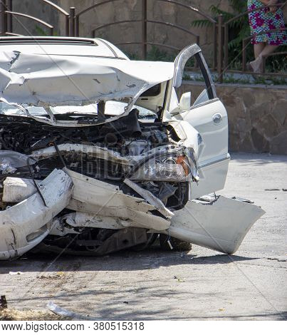 Close Up Of A White Car Wrecked During A Car Accident. Damaged Front Bumper, Engine, Headlights. Inj