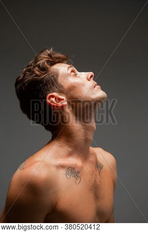 Portrait Of Handsome Young Guy With Stylish Haircut Without Shirt Standing In Studio. Body With Tatt