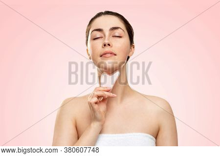 Gua Sha Massage. Portrait Of A Woman In A Bath Towel, Closing Her Eyes, Makes A Guasha Massage In Th