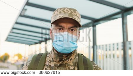 Portrait Of Serious Caucasian Handsome Young Male Soldier In Cap And Medical Mask Standing At Street