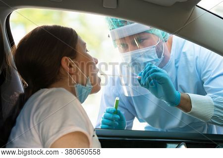 Woman getting tested at a coronavirus drive thru station by medical staff with PPE suit by throat swab. Health care drive thru service and medical concept