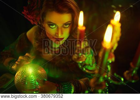 Bewitching fortune teller woman reading future on magical crystal ball.