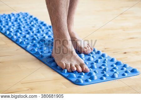 man doing flatfoot correction gymnastic exercise walking on massage mat at home