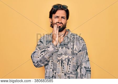 Young handsome hispanic bohemian man wearing hippie style and sunglasses touching mouth with hand with painful expression because of toothache or dental illness on teeth. Dentist