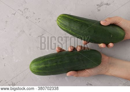 Two Large Ripe Cucumbers In Girls Hands On A Gray Background, Closeup, View From Above