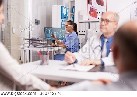 Nurse In Blue Uniform Holding X-ray Image In Hospital Cabinet. Older Doctor Wearing White Coat Durin