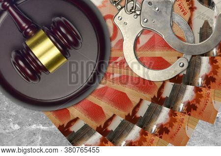 50 Canadian Dollars Bills And Judge Hammer With Police Handcuffs On Court Desk. Concept Of Judicial 