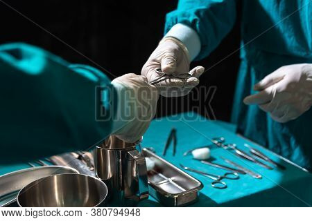 Two Surgeons Working In Operating Room, One Hand Over Surgical Equipment To Another. Surgeons Hands 