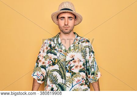 Young handsome man with blue eyes on vacation wearing summer florar shirt and hat with serious expression on face. Simple and natural looking at the camera.