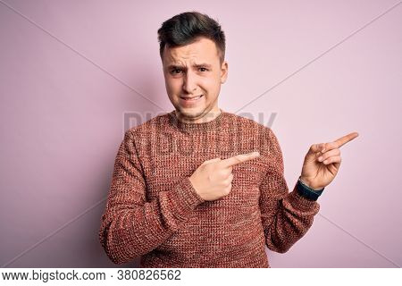 Young handsome caucasian man wearing casual winter sweater over pink isolated background Pointing aside worried and nervous with both hands, concerned and surprised expression