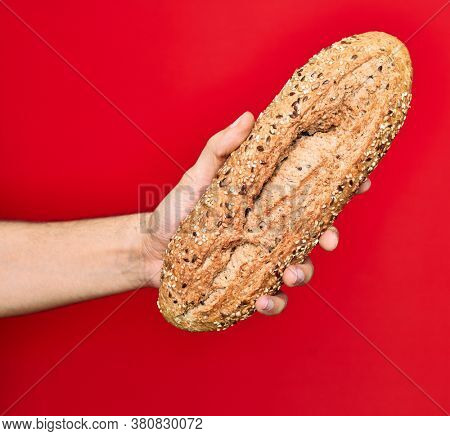 Beautiful hand of man holding wholemeal integral bread with cereals over isolated red background