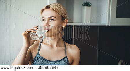 Young Fitness Lady Drinking Water After Yoga Exercises Wearing Sportswear At Home In The Kitchen