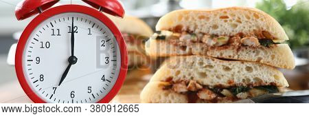 Close-up Of Red Clock Showing Seven In Morning. Hot Sandwich With Tasty Stuffing On Table. Quick Bre