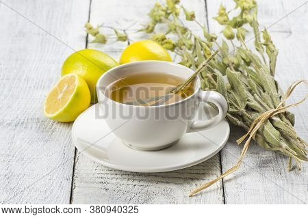 White Cup Of Herbal Sage Tea With Dried Sage Leaves And Lemon On White Wooden Rustic Background. Her