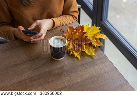 Young Woman In Cafe Whriting Text Message From Her Mobile Phone. Autumn Still Life With Cappuccino C