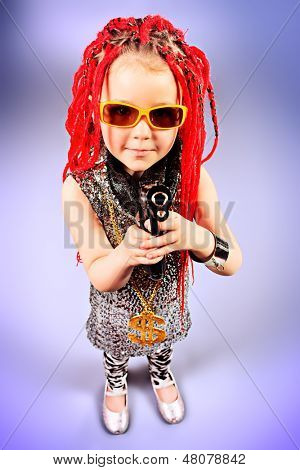 Porträtt av en trendig liten tjej bär röda flätor och moderna kläder och hålla en pistol. 