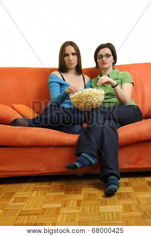 female friends eating popcorn and watching tv at home on orange sofa isolated on white