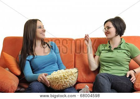 female friends eating popcorn and watching tv at home on orange sofa isolated on white