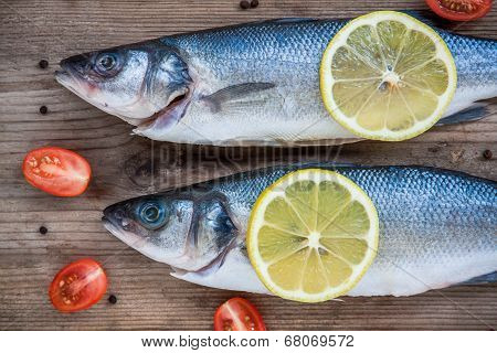 Two Raw Seabass Fish With Lemon And Cherry Tomatoes On Wooden Background