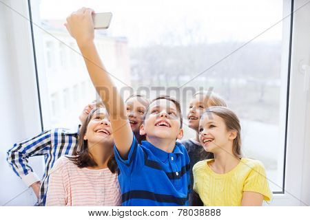 education, elementary school, drinks, children and people concept - group of school kids taking selfie with smartphone in corridor