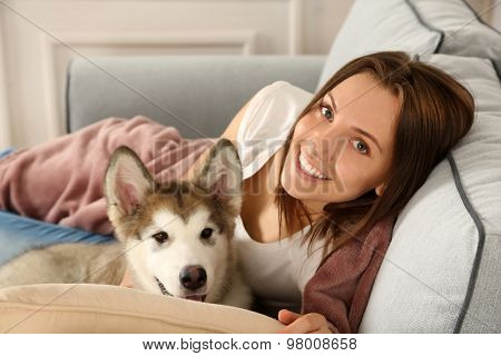 Young woman lying with malamute dog on sofa in room