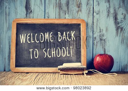 a chalkboard with the text welcome back to school written in it, a piece of chalk, an eraser and a red apple on a rustic wooden table, cross processed