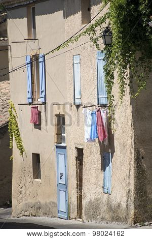 Typical House In South France With Blue Shutters And Drying Laundry Outside The Windows