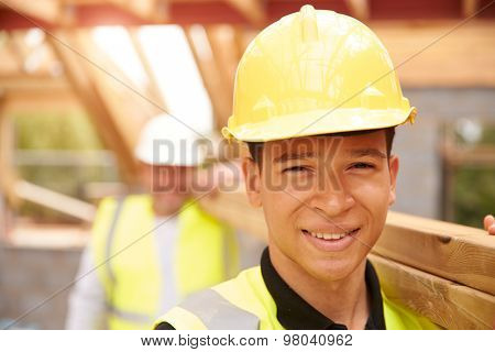 Portrait Of Builder And Apprentice Carrying Wood On Site