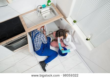 Repairman Fixing Pipe While Woman Squeezing Wet Cloth