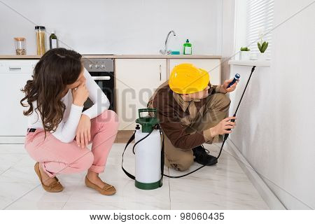 Woman Looking At Worker Spraying Insecticide Under Windowsill