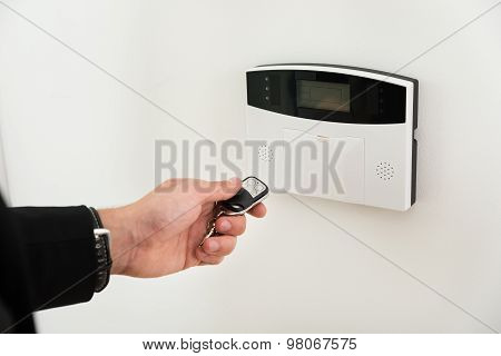 Hands With Remote Control In Front Of Security System