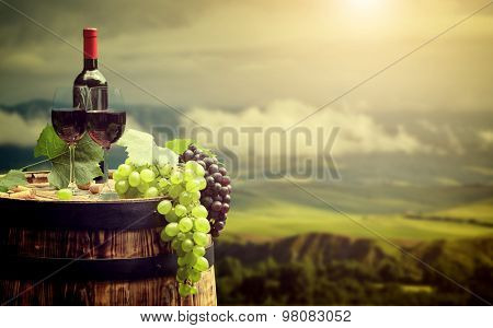 Red wine bottle and wine glass on wodden barrel. Beautiful Tuscany background