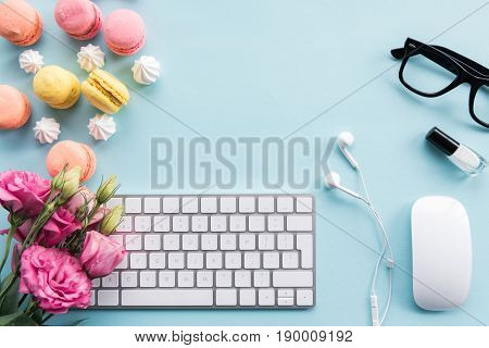 top view of keyboard macarons eyeglasses earphones and flowers isolated on blue