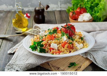 Tabula. Bulgur with baked pepper tomato and feta cheese on an old wooden background. Selective focus.
