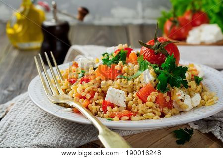 Tabula. Bulgur with baked pepper tomato and feta cheese on an old wooden background. Selective focus.