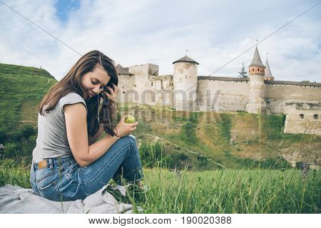 yang pretty tourist sits on rock in front of old castle and eat aplle