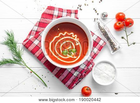 Hot bowl of tomato basil soup with mayo, squared rustic napkin, salt and pepper, topview
