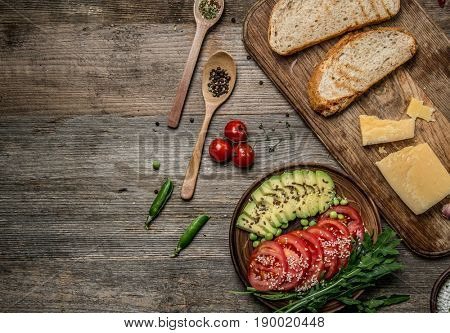 Tasty appetizers, avocado and cut tomatoes sitting on dark wooden table, topview, textspace