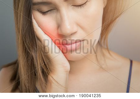 Suffering from toothache. Beautiful young woman suffering from toothache while standing against grey background
