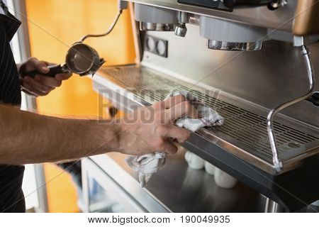 Mid section of waiter cleaning coffeemaker machine in cafÃÂ©