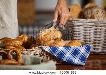 Mid-section of staff holding bread with tong in bakery shop