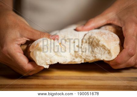 Mid section of male staff tearing a bun in bakery shop