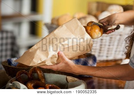 Mid-section of staff packing bread in paper bag at bakery shop