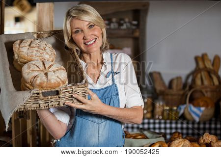 Female staff holding basket of sweet foods in bakery section of supermarket